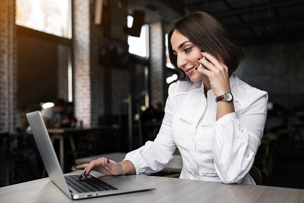 Mulher em um escritório trabalhando com SAP B1 HANA em seu notebook e falando no celular